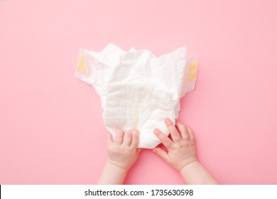 Baby hands touching white diaper on light pink table background. Pastel color. Closeup. Point of view shot.