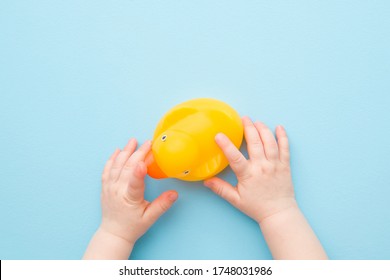 Baby hands touching yellow rubber duckling on light blue table background. Pastel color. Closeup. Bathing toy for little kids. Point of view shot.