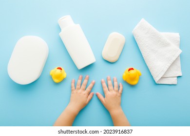 Baby hands, white shampoo bottle, soap bar, towel, wisp and yellow rubber ducks on light blue table background. Pastel color. Closeup. Point of view shot. Things for baby bathing. 