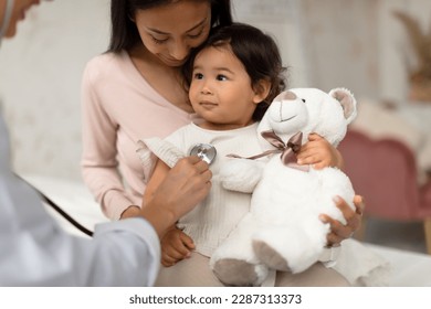 Baby Health Check Up. Korean Mom And Infant Daughter Having Medical Appointment, Unrecognizable Doctor Listening To Little Girl's Heart Putting Stethoscope To Her Chest In Modern Clinic Indoors - Powered by Shutterstock