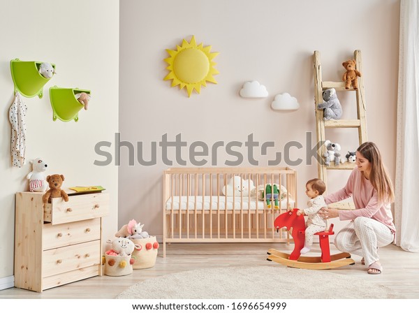 部屋にいる赤ちゃんと母親 ベッドとピンクの椅子のおもちゃと階段のデコールを使った装飾的なインテリアスタイル の写真素材 今すぐ編集
