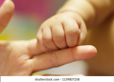 Baby holding finger of his mother giving senses of attachment and bonding. The image taken with a selective focus stressing an emotional scene.