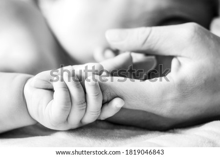 A baby is holding on to the mother's finger. Hands close-up. Black and white photo. Concept of motherhood and children's day