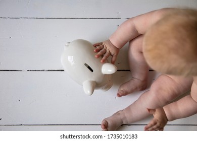 A Baby Holding Onto A Piggy Ban Money Box. Childcare Costs Concept