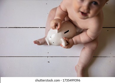 A Baby Holding Onto A Piggy Ban Money Box. Childcare Costs Concept