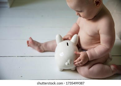 A Baby Holding Onto A Piggy Bank. Cost Of Raising A Child Concept