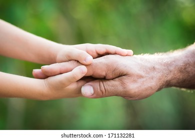 Baby holding senior man by the hands outdoors