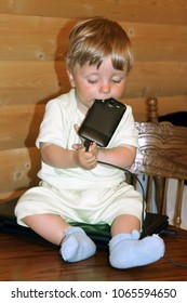 Baby Infant Boy Sits On A Desk On A Laptop And Holds A Cell Phone In His Mouth. Stay At Home. Coronavirus COVID-19 Quarantine