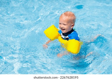 Baby with inflatable armbands in swimming pool. Little boy learning to swim in outdoor pool of tropical resort. Swimming with kids. Healthy sport activity for children. Sun protection. Swim aids. - Powered by Shutterstock