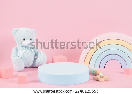Baby kid toys background. Empty round podium platform stand and blue teddy bear, pastel color rainbow and wooden educational toys on pastel pink background. Front view