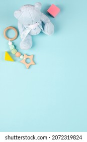 Baby kids toys background with teddy bear, wooden blocks and organic teether on light blue background. Top view, flat lay