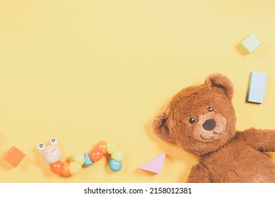 Baby Kids Toys Frame With Teddy Bear, Wooden Toy, Colorful Cubes On Pastel Yellow Background. Top View