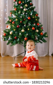 Baby In A Knitted Red And White Onesie In Front Of A Christmas Tree