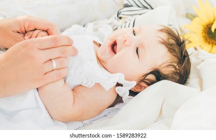 Baby laying on the bed with caring touch of mother's hands. Nursery for children. - Shutterstock ID 1589283922