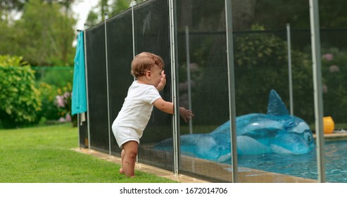 
Baby Leaning On Swimming Pool Fence Protection. Infant Standing On Safety Gate