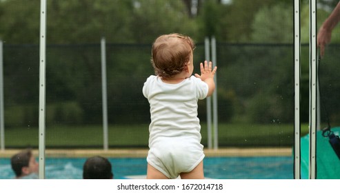 
Baby Leaning On Swimming Pool Fence Protection. Infant Standing On Safety Gate