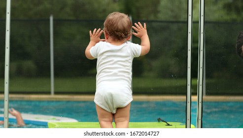 
Baby Leaning On Swimming Pool Fence Protection. Infant Standing On Safety Gate