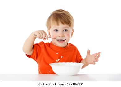 Baby learning to feed herself - eating the oatmeal with a spoon, isolated on white