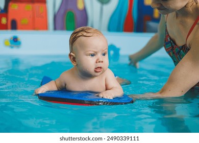 A baby learns to swim with a coach in the pool. Swimming courses for small children. Swimming pool for children - Powered by Shutterstock