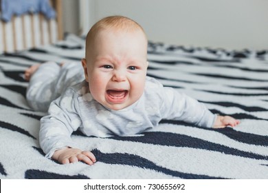 the baby lies on the bed and cries. Portrait of crying baby. Unhappy uncomfortable shirtless newborn baby lying and crying on the bed