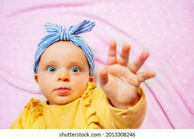 Baby Lift Up Palm Reaching With Hand Stop Gesture Wear Blue Bow Lay On The Pink Blanket View From Above