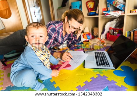 baby looking at camera while his mother works on the computer, concept of woman's work-life balance.