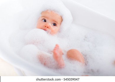 Baby looking upwards in a plastic tub full of foam.