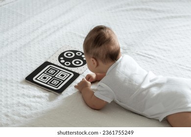 A baby looks at a black and white contrast educational book. Intellectual development of newborns. Developing cards for children.