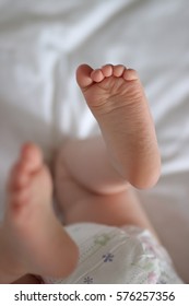 Baby Lying Down On White Bed Sheet With Feet In The Air