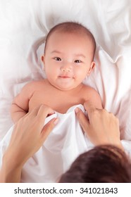 Baby Lying On Bed At Home. Mom Putting A Blanket On Her Baby.