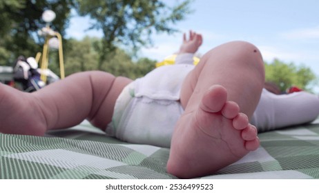 Baby lying on blanket outdoors, feet raised in the air. The playful moment captures the joy and curiosity of early childhood in an open, natural park environment - Powered by Shutterstock