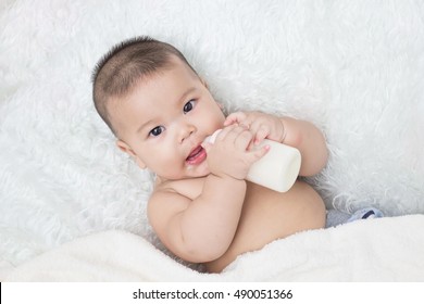 Baby lying on the white carpet and drinking milk from a bottle.