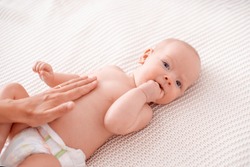 Baby Massage. Masseur Massages Baby's Tummy During Colic. Newborn With Colic Without Clothes Is Lying On His Back, Mother's Hand On His Stomach Helps Her Cope With Colic. Hand In His Mouth, Teething.