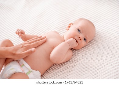 Baby Massage. Masseur Massages Baby's Tummy During Colic. Newborn With Colic Without Clothes Is Lying On His Back, Mother's Hand On His Stomach Helps Her Cope With Colic. Hand In His Mouth, Teething.