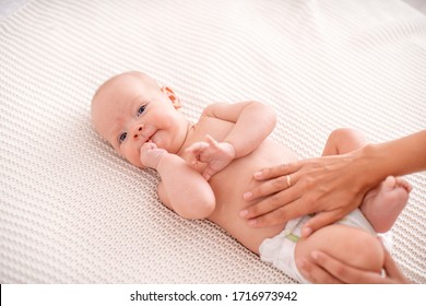 Baby massage. Masseur massaging tummy of baby during colic. Newborn colicky baby without clothes laying on her back, mother's hand on her tummy helping her with colic. - Powered by Shutterstock