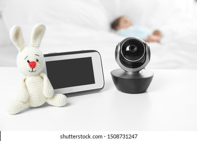 Baby Monitor, Camera And Toy On Table Near Bed With Child In Room. Video Nanny