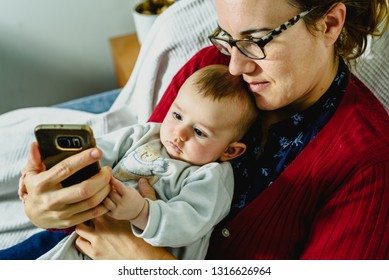 Baby On The Arms Of His Mother Playing With A Mobile Phone To Explore The Virtual World.