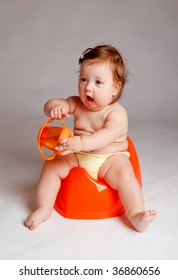 Baby On Orange Potty With Orange Bottle In Hands