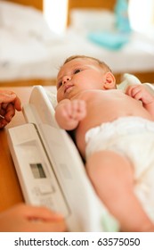 Baby On A Weight Scale, Her Mother Or A Doctor Is Checking Health And Development Of The Newborn