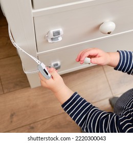 Baby Opens The Child Lock On The Closed Drawer Of The Cabinet. Toddler Baby With Hand Opens Door Lock On Chest Of Drawers. Kid Aged One Year And Three Months