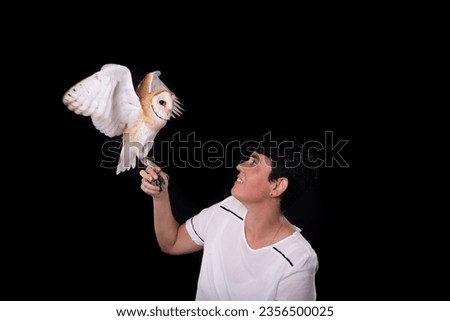 A baby owl with its wings outstretched held by a woman. Wild animal. Studio photo with black color background.