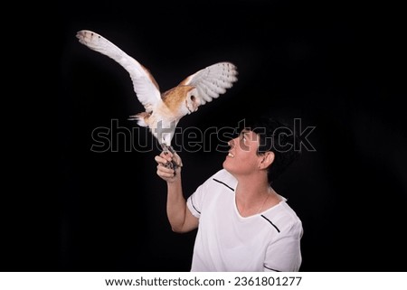 A baby owl with its wings outstretched held by a woman. Wild animal. Studio photo with black color background.