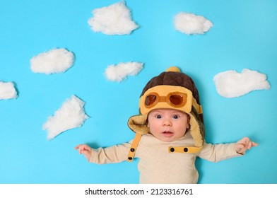 Baby In A Pilot's Helmet Against An Artificial Sky And Cotton Wool Clouds.