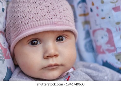 A Baby In A Pink Cap With Black Eyes