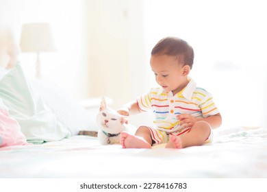 Baby playing with cat. Kid holding kitten. Little Asian boy and his pet. Animal care. Child on white bed in sunny bedroom at home. Kids play with pets. Children and domestic animals. - Powered by Shutterstock