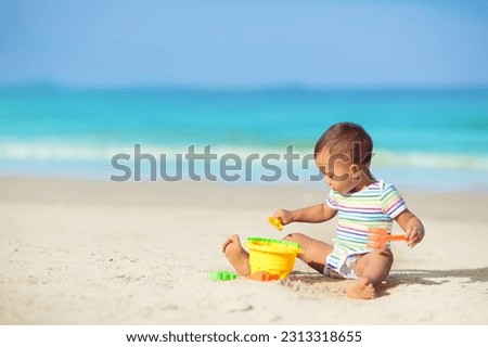 Baby playing on tropical beach. Children play at sea on summer family vacation. Sand and water toys, sun protection for young kids. Little boy digging sand, building castle at ocean shore.