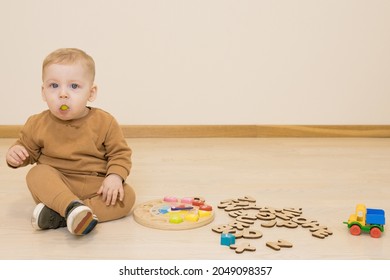 Baby Plays With Educational Wooden Toys On The Floor. Toddler Has Wooden Letter Of English Alphabet In His Mouth. Concept Of Early Study Of Languages, Kid Takes Toys In His Mouth, Danger Of Choking.