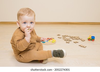 Baby Plays With Educational Wooden Toys On Floor. Toddler Has Small Part Of The Toy In His Mouth. Concept Of Early Study Of Languages, Kid Takes Toys In His Mouth, Danger Of Choking, Child Development