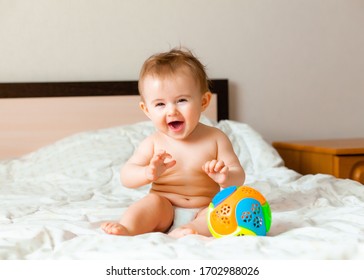 Baby plays with a multi-colored ball on the bed in the children's room - Shutterstock ID 1702988026