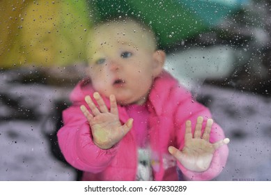 Baby Pressing Hands Against The Window With Rain Drops